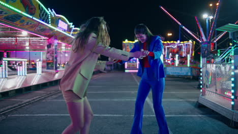 joyful girls dancing amusement park street. happy friends having fun at night.