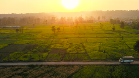 Das-Drohnenvideo-Zeigt-Einen-Lastwagen,-Der-Eine-Straße-Inmitten-Eines-Wunderschönen-Senffelds-Zur-Goldenen-Stunde-In-Der-Terai-Ebene-Von-Nepal-überquert