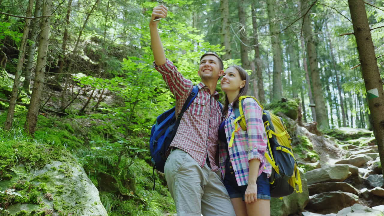 un atractivo par de turistas son fotografiados en el bosque selfie con mochilas en una caminata 4k v