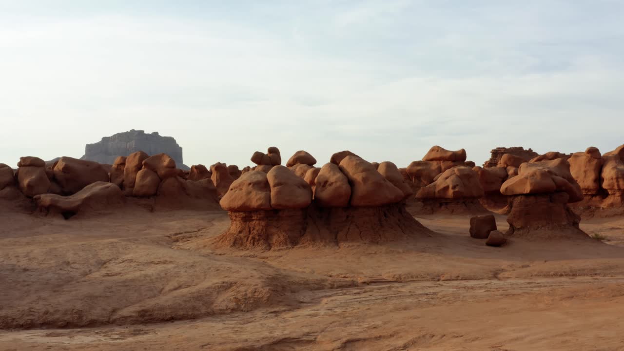 아름다운 고블린 밸리 유타 주립 공원의 공중 드론 샷에 있는 화려한 돌리는 따뜻하고 화창한 여름날 배경에 큰 빨간 버트가 있는 이상한 버섯 암석에 접근하고 있습니다.