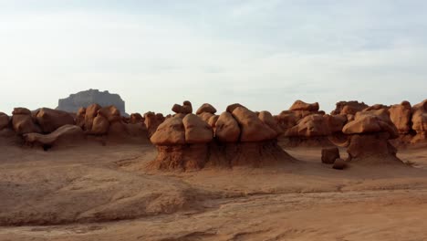 gorgeous dolly in aerial drone shot of the beautiful goblin valley utah state park approaching strange mushroom rock formations with a large red butte in the background on a warm sunny summer day