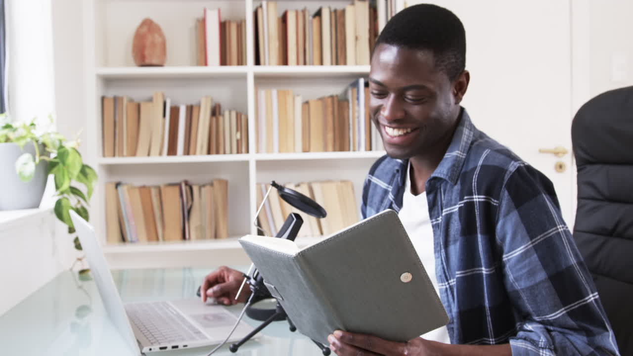 Man reading book and using laptop at home, smiling and enjoying leisure time