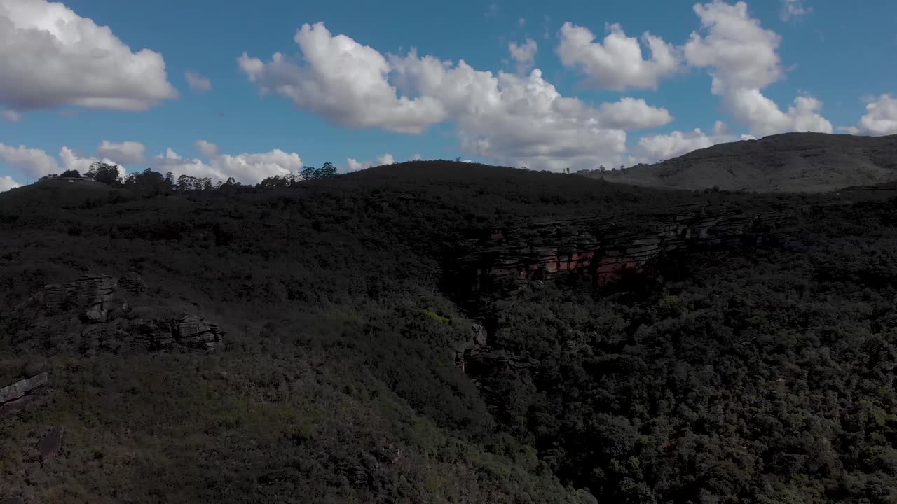 Aerial descend showing a blue sky with clouds and a rock plateau forest landscape in the Andorinhas [Swallows] park near Ouro Preto, Brazil