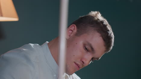 close-up of young man in white shirt looking downwards while holding cue stick. focused expression suggests deep thought or concentration. soft lighting enhances atmosphere