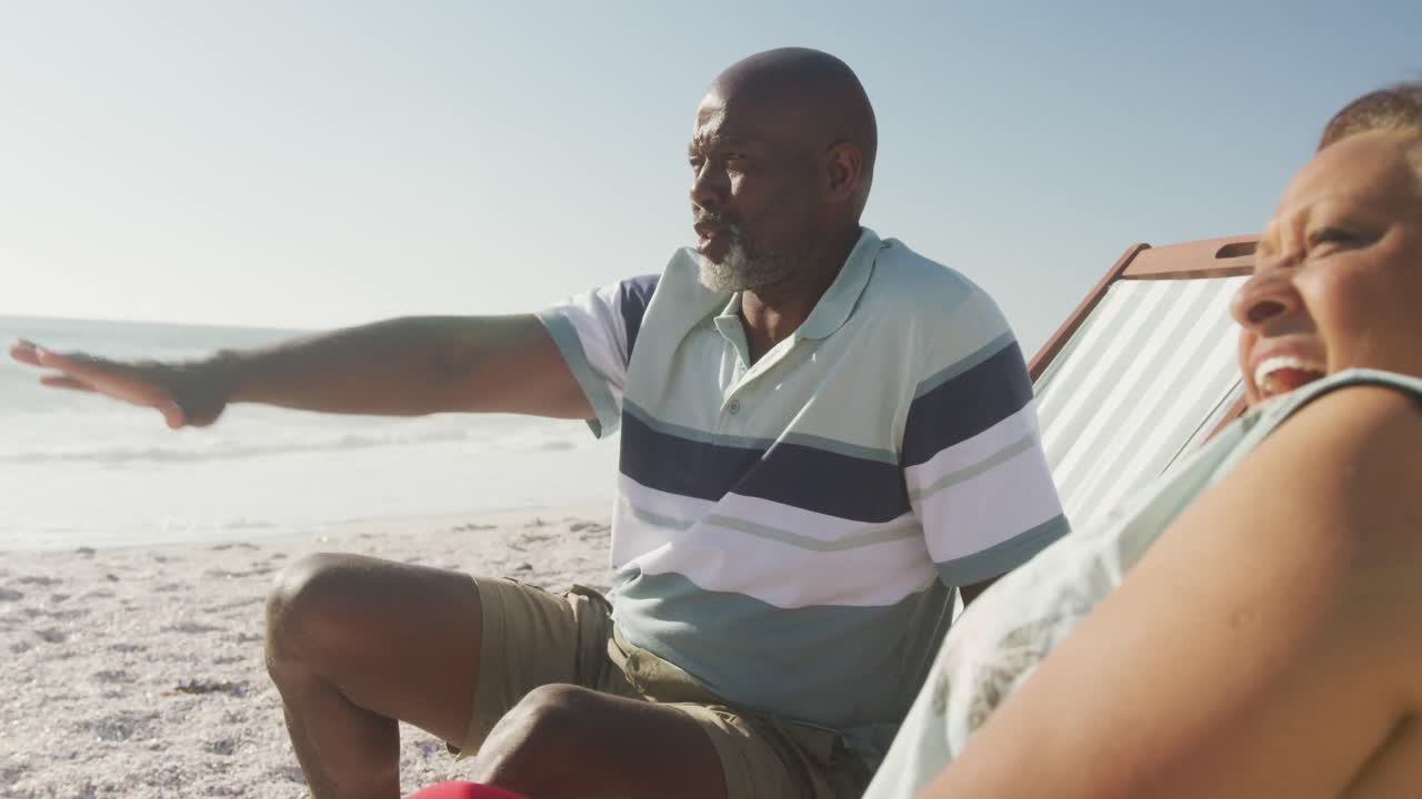 Smiling senior african american couple lying on sunbeds on sunny beach