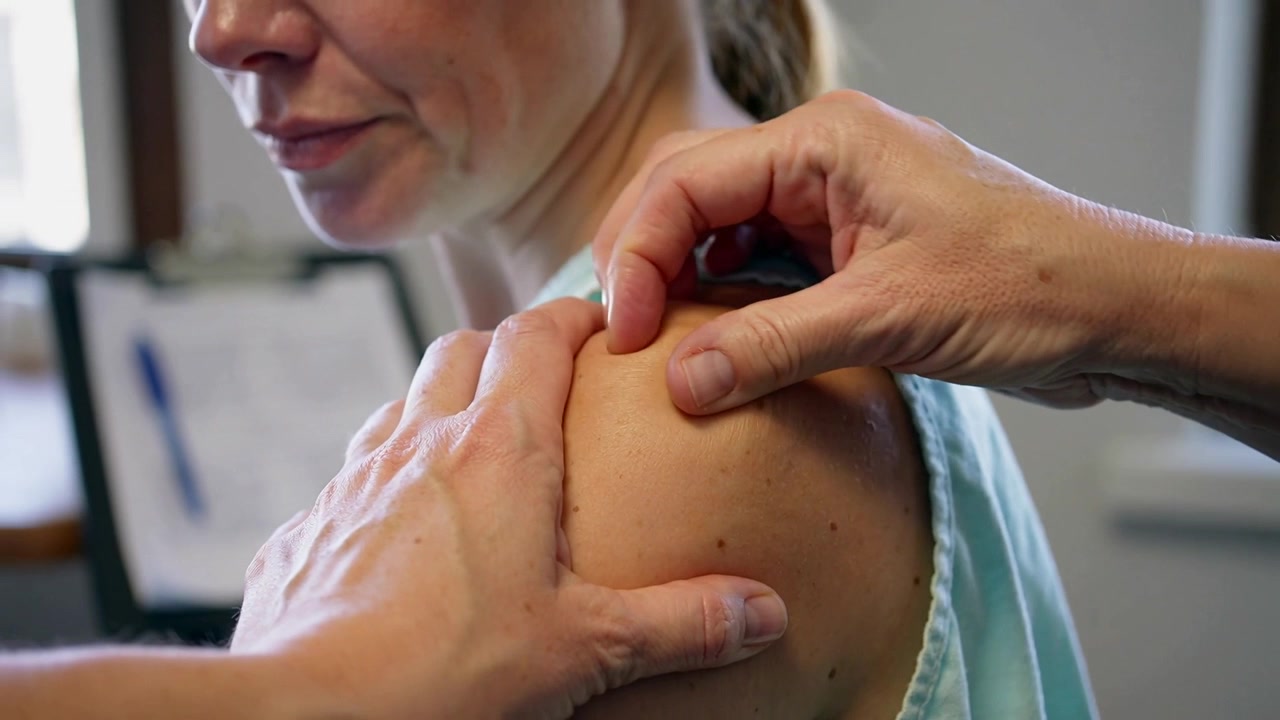 Terapeuta massageia e avalia o ombro direito de paciente de regata na clínica.