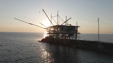 Aerial-view-of-a-trabucco-silhouette,-a-traditional-fishing-machine,-on-the-italian-coastline,-at-sunset