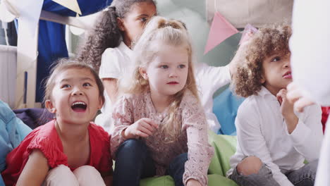 infant school kids sitting on bean bags in a comfortable corner listening their teacher, close up