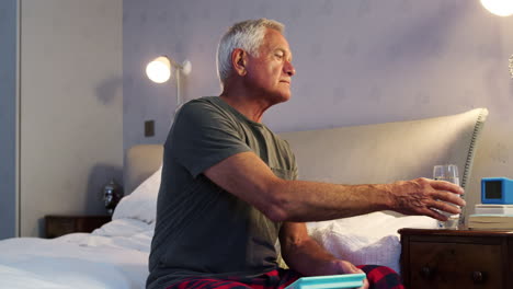 Senior-Man-Sitting-On-Bed-At-Home-Taking-Medication