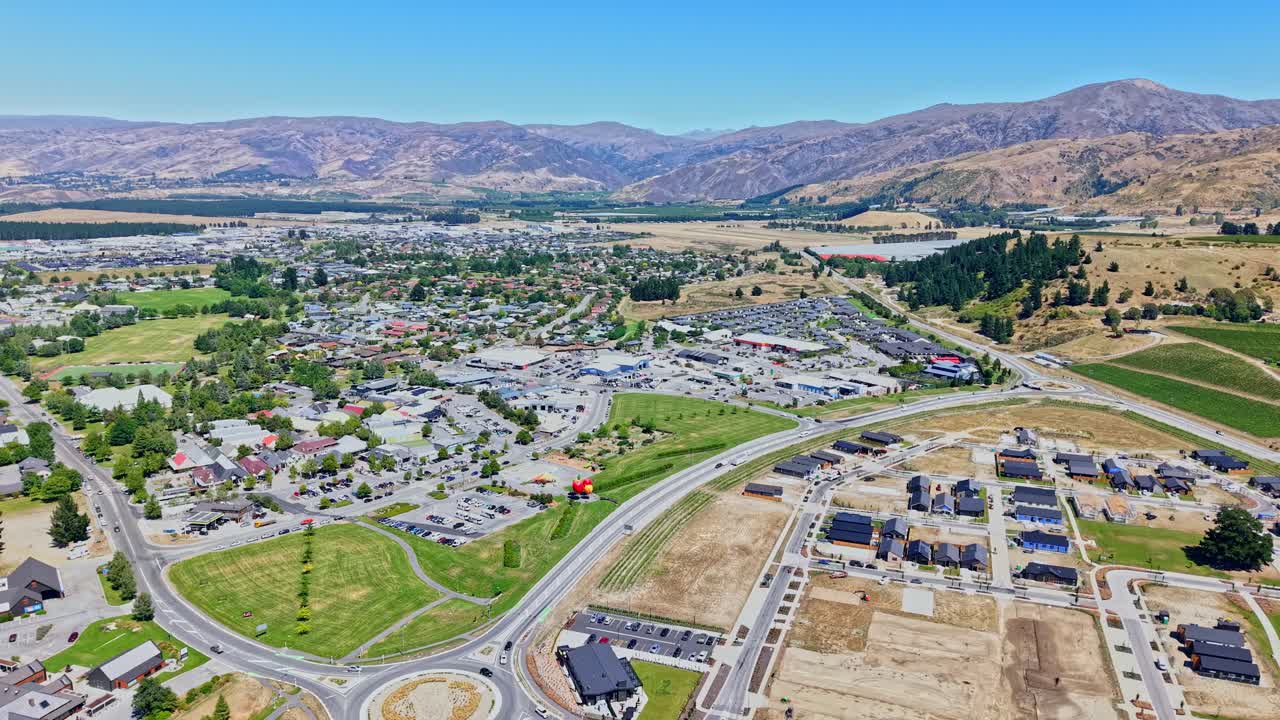 Scenic Aerial backward drone shot over Cromwell, New Zealand. Sunny day view of the giant fruit landmark, fruit-farm town, blue sky, and mountains in the background
