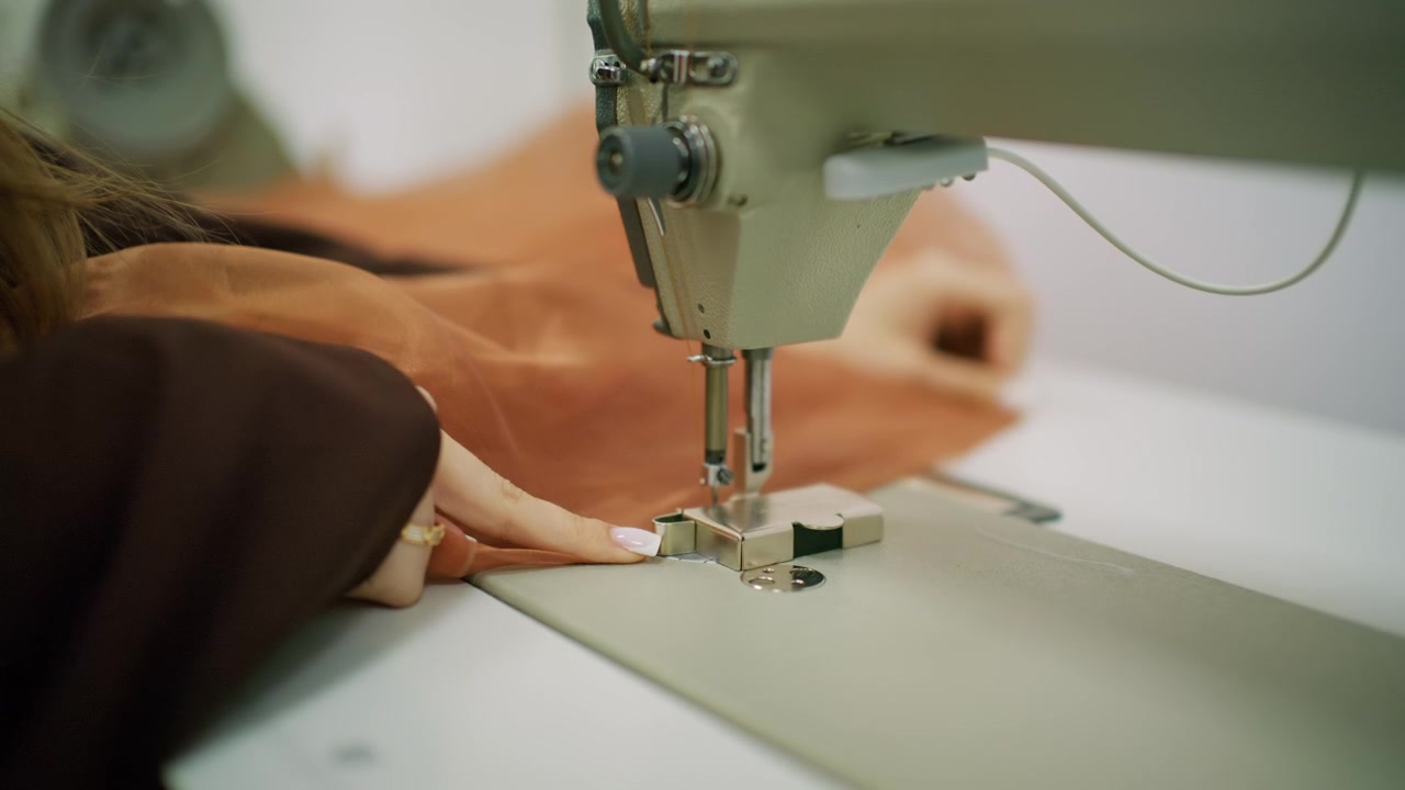 Close up of a person guiding brown sheer fabric under the needle of an industrial sewing machine