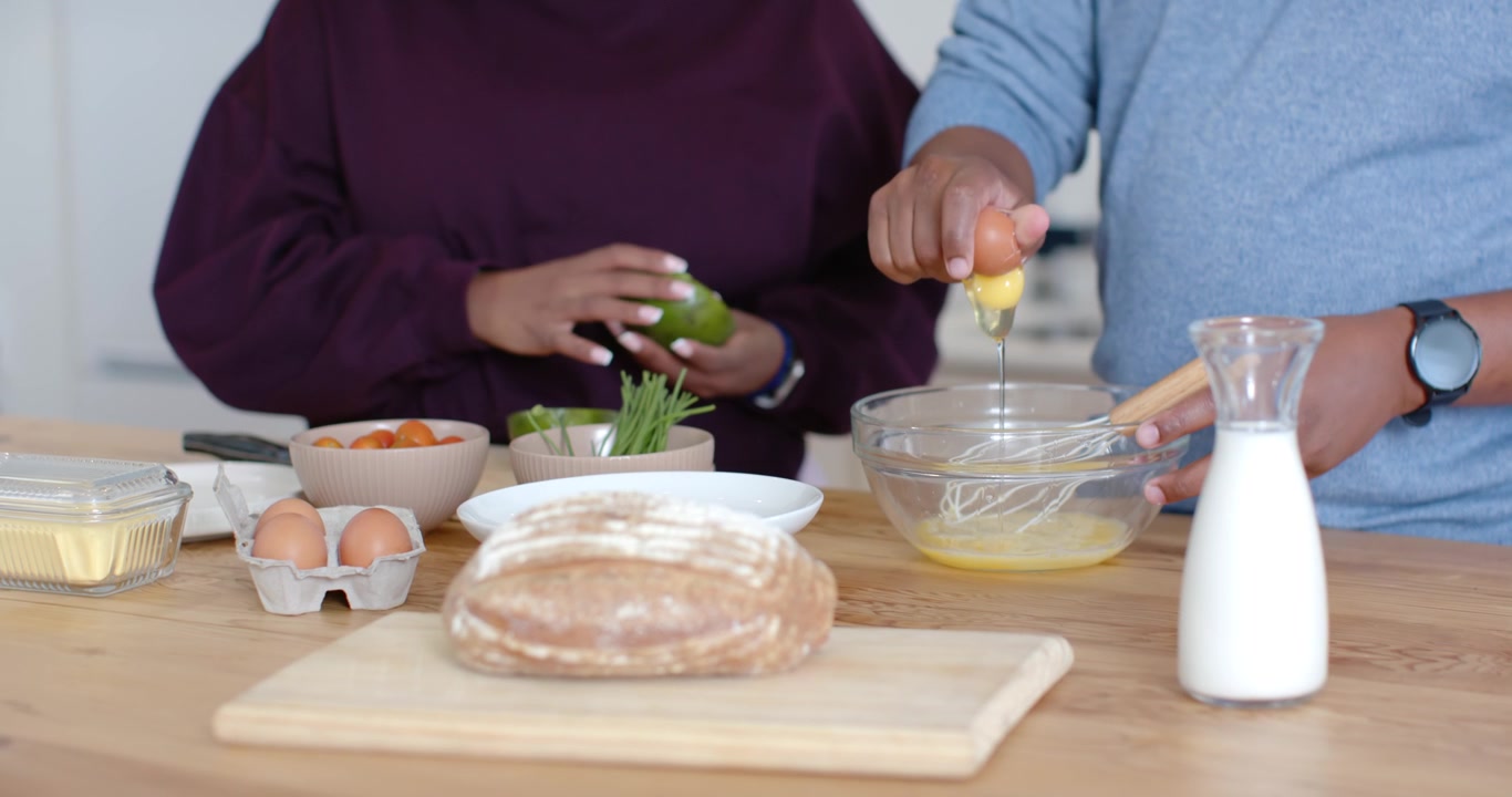 African American couple making breakfast at counter, woman pitting avocado while man whisking eggs
