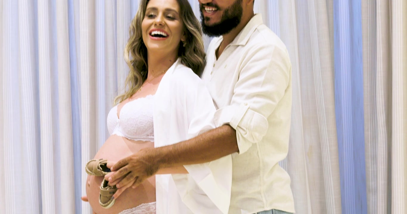 Happiness of couple to daddy put baby shoes on pregnant mama's belly.