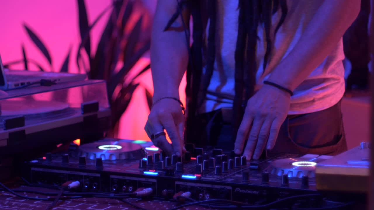 dj con dreadlocks remezclando música usando un tocadiscos durante una actuación en vivo, filmado como un primer plano en la parte inferior del cuerpo