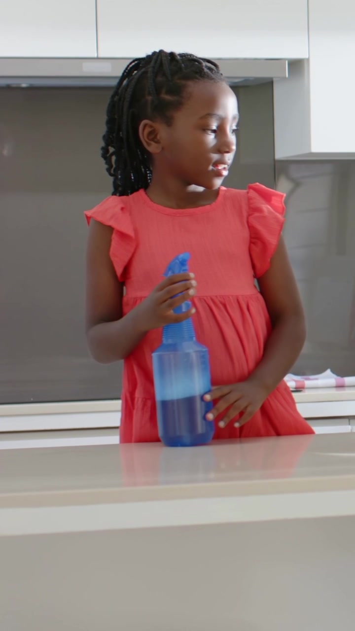 Video verticale: Una ragazza in abito color corallo entra in cucina, afferra uno spruzzino, risponde, con spazio per il testo.