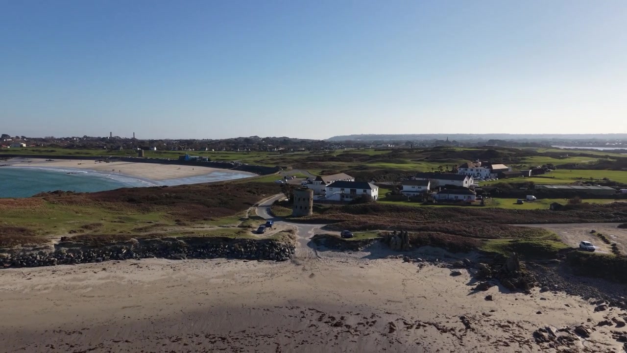 Torre Martello Pembroke Vale Guernsey. Volo di drone ad alta quota sopra la Torre Martello con vista sulla spiaggia di Lancresse Bay e sulla Common sotto il sole del tardo pomeriggio con cielo azzurro limpido