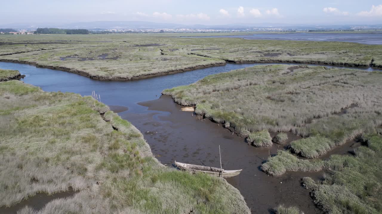 un barco de madera abandonado descansa en una estrecha vía fluvial en medio de las verdes marismas de estarreja, aveiro, portugal - aero