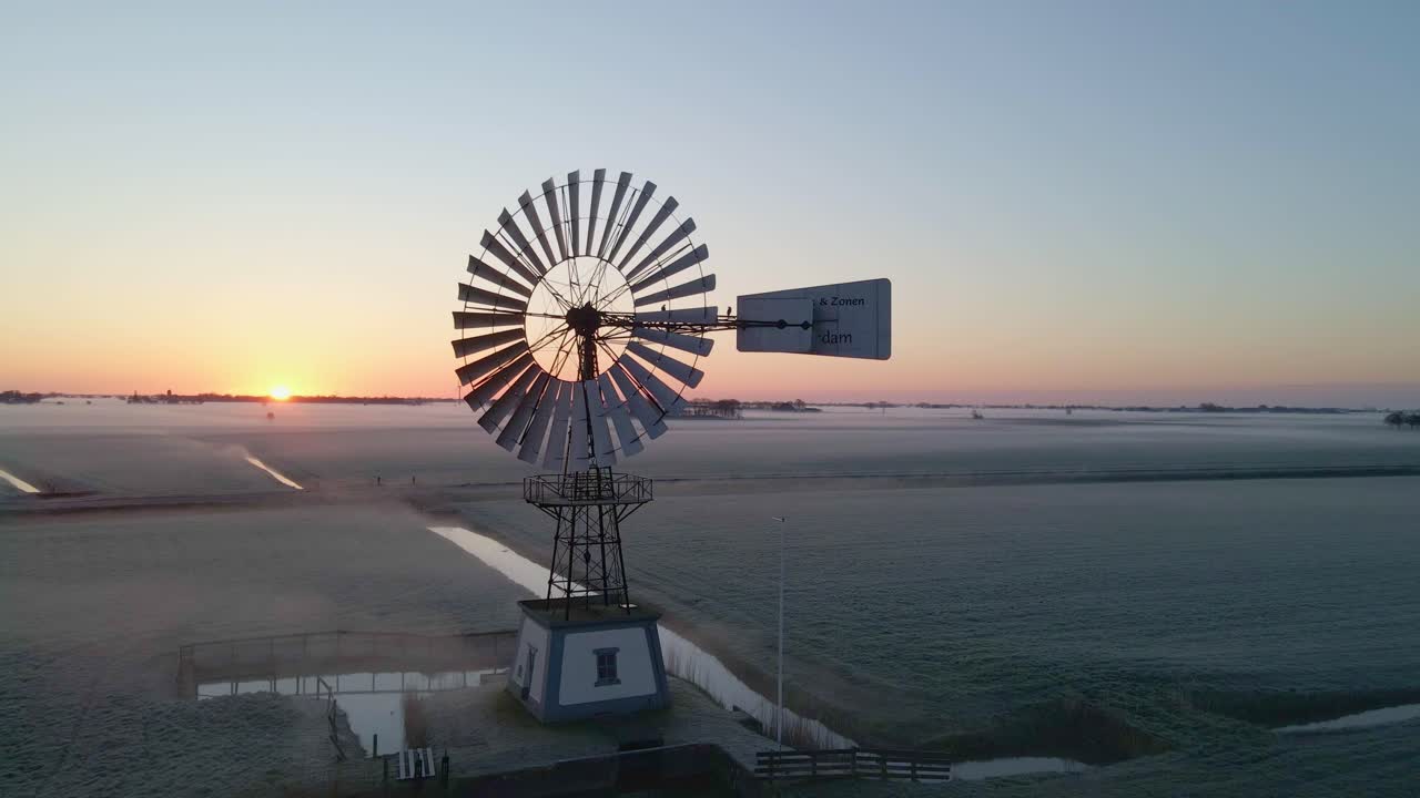 L'alba nebbiosa mette in risalto un mulino a vento americano in un campo erboso, Frisia, Paesi Bassi