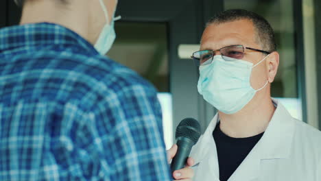un reportero con una máscara protectora entrevista a un médico a la entrada del hospital