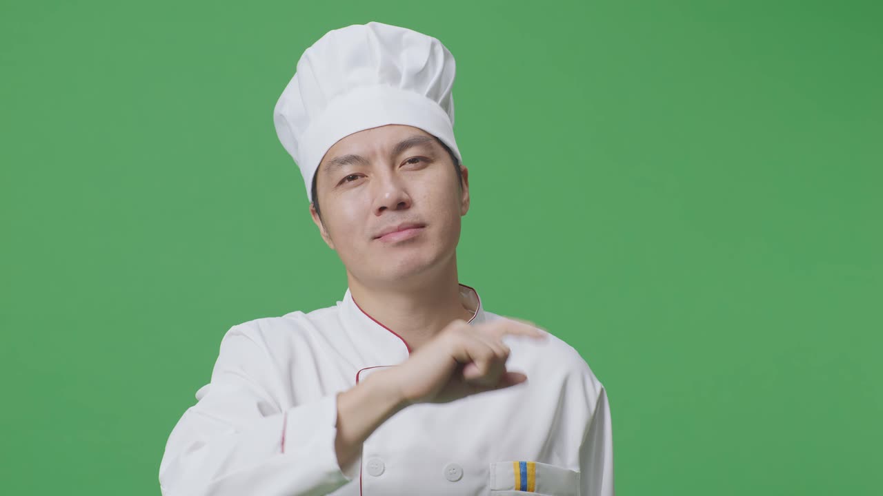 아시아 남성 요리사가 미소 짓고 가을 만지며 녹색 스크린 배경 스튜디오에 서있는 동안 당신을 가리키고 있습니다.