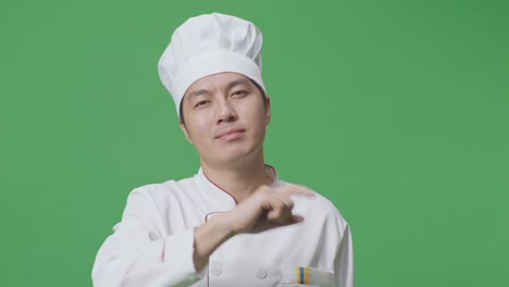 primer plano del chef asiático sonriendo y tocando su pecho luego señalándote mientras está de pie en el estudio de fondo de la pantalla verde