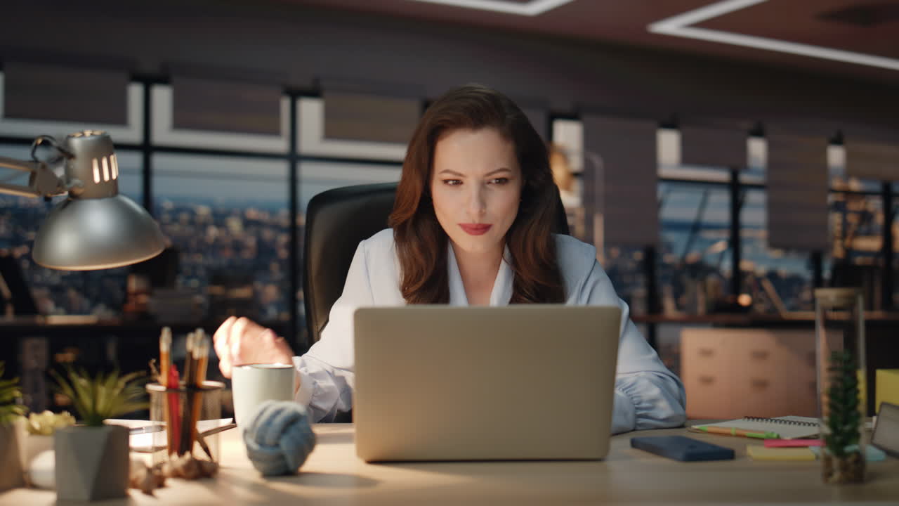 Donna soddisfatta che si gode un cappuccino in primo piano sul posto di lavoro notturno. Donna che sorseggia caffè.