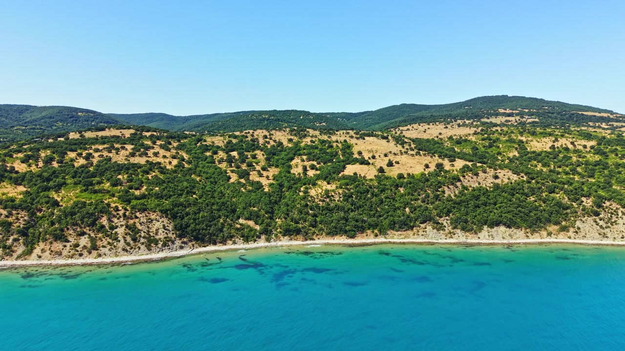 Vista di una costa con colline verdi e acqua azzurra durante il giorno in un'ambientazione estiva.