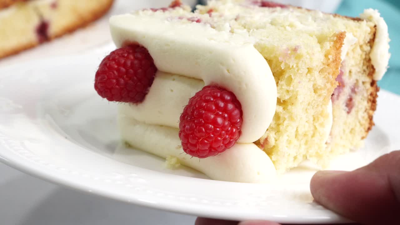 Making a dessert called Red Raspberry Tea Cake made with fresh berries and vanilla buttercream frosting. Great for Tea Parties. Cutting a piece of raspberry dessert on a plate with closeup view
