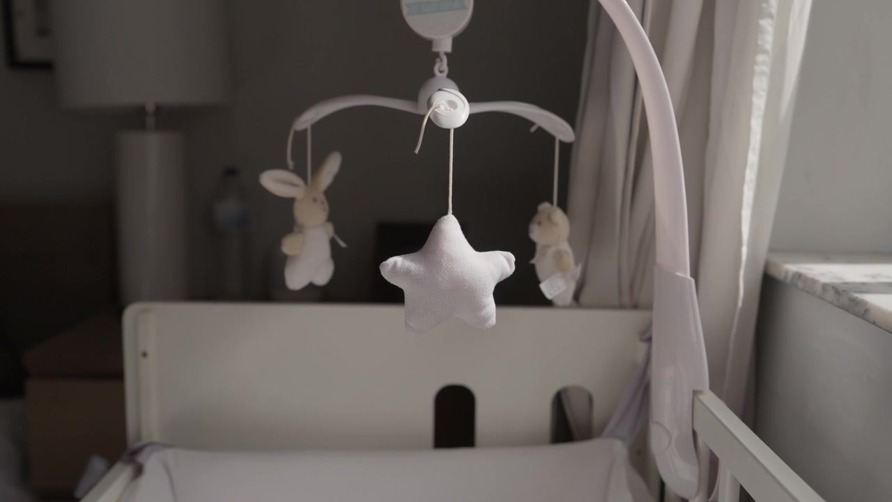 Plush bunny star and bear hanging from a cot mobile above an empty white baby crib