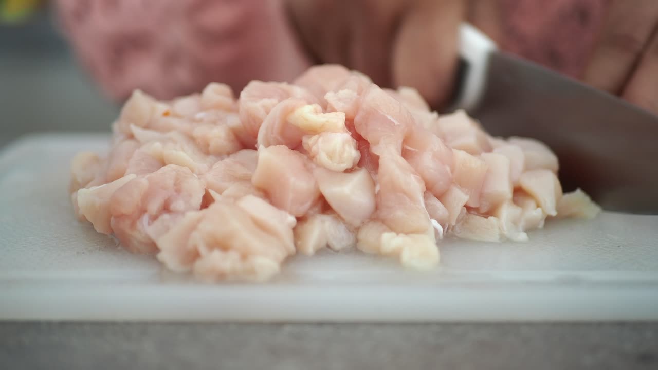 primer plano de las manos cortando pecho de pollo crudo en la tabla de cortar