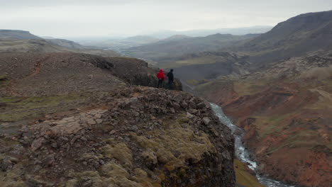 Drohnenblick-Menschen-Wanderer-Stehen-Oben-Auf-Einer-Klippe-Und-Sehen-Ein-Atemberaubendes-Panorama-In-Island.-Luftbild-Zwei-Touristen-Betrachten-Das-Erstaunliche-Landmannalaugar-Tal-Mit-Dem-Fossa-Fluss,-Der-Das-Moosige-Hochland-Fließt