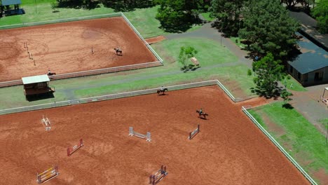 wide equestrian training area with multiple horses and obstacles in separate fenced sections.