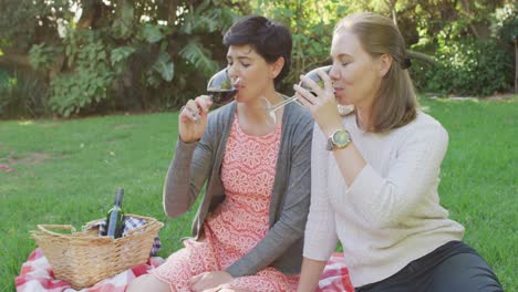 pareja de lesbianas caucásicas bebiendo vino juntos en el jardín durante un picnic