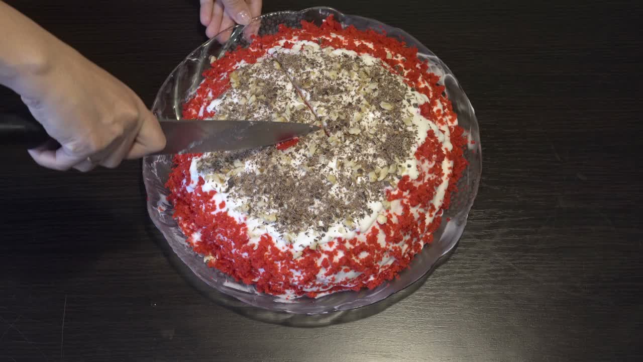 여자는 검은 테이블 위의 유리 접시 위에 서있는 색 크림으로 아름다운 은 케이크를 조각으로 잘라기 시작합니다.