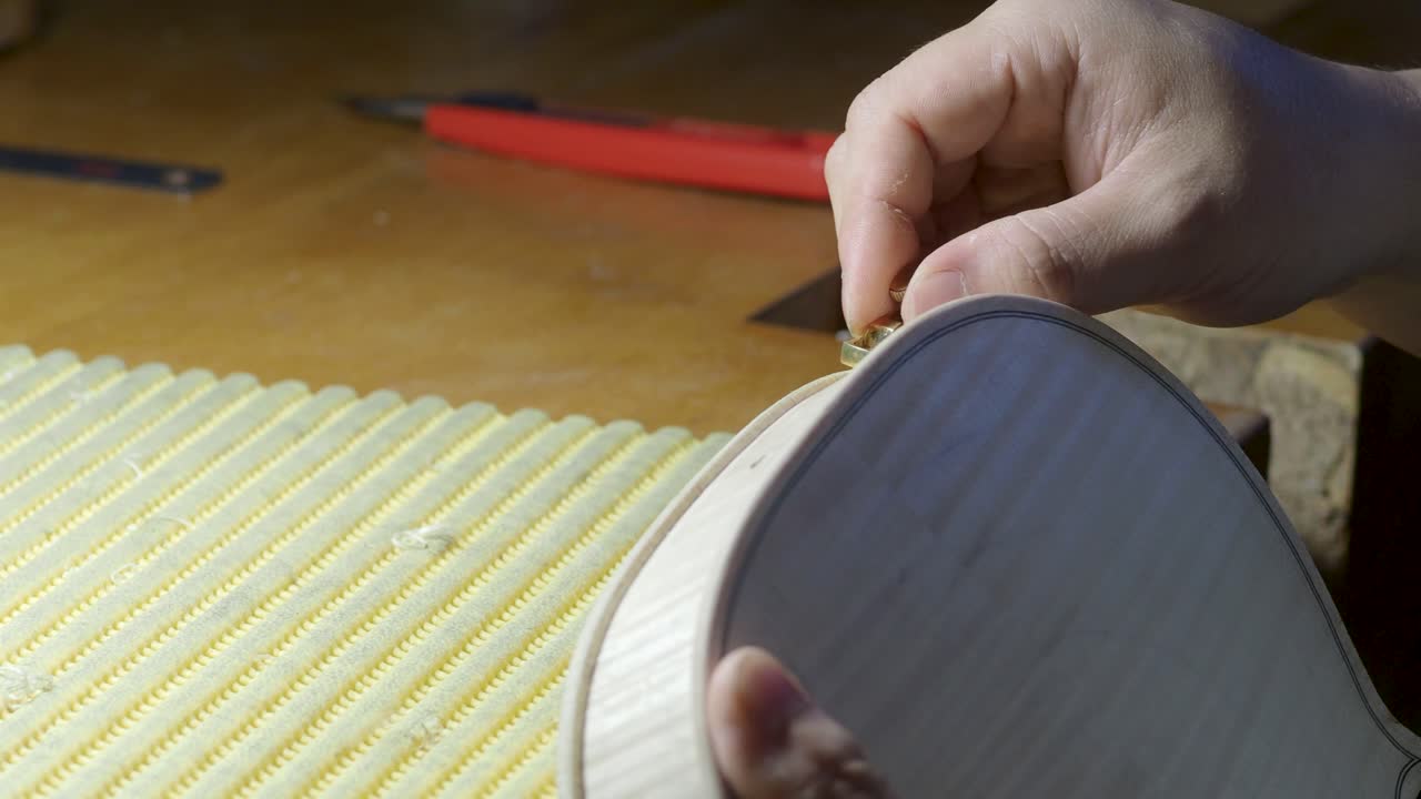 macro close up of artisan luthier maker work on new classic handmade raw violin smooth edge in waist and purfling rasp in workbench of workshop in Cremona Italy 4k video