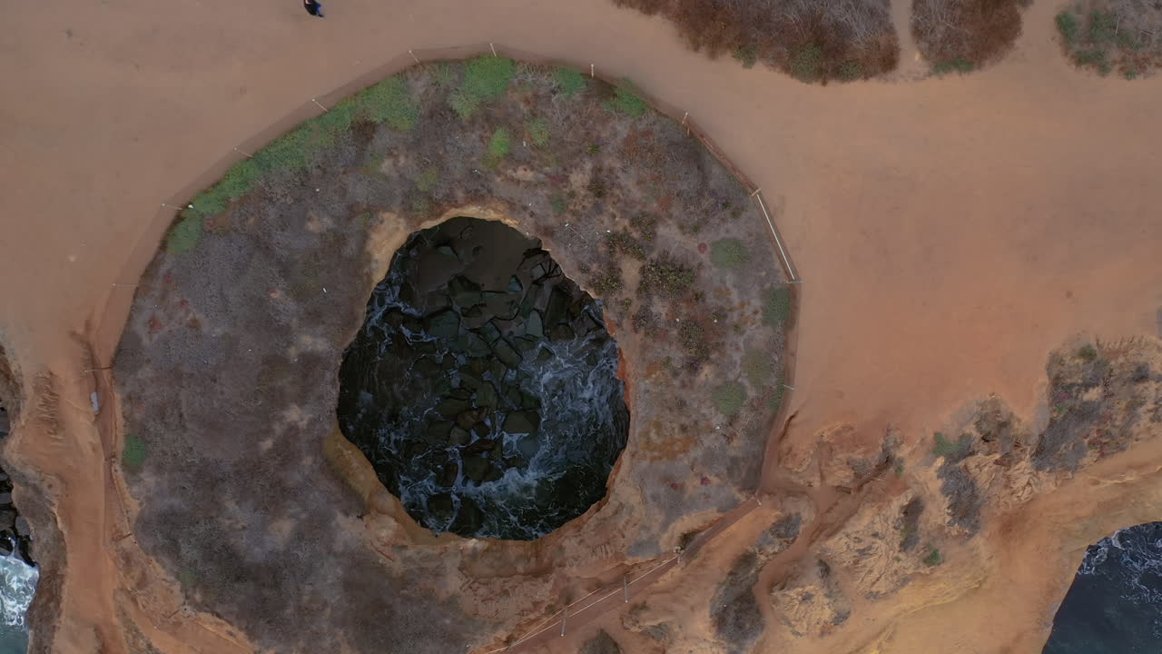 ojo de pájaro aéreo descendiendo sobre un agujero de arenisca erosionado, acantilados al atardecer, california