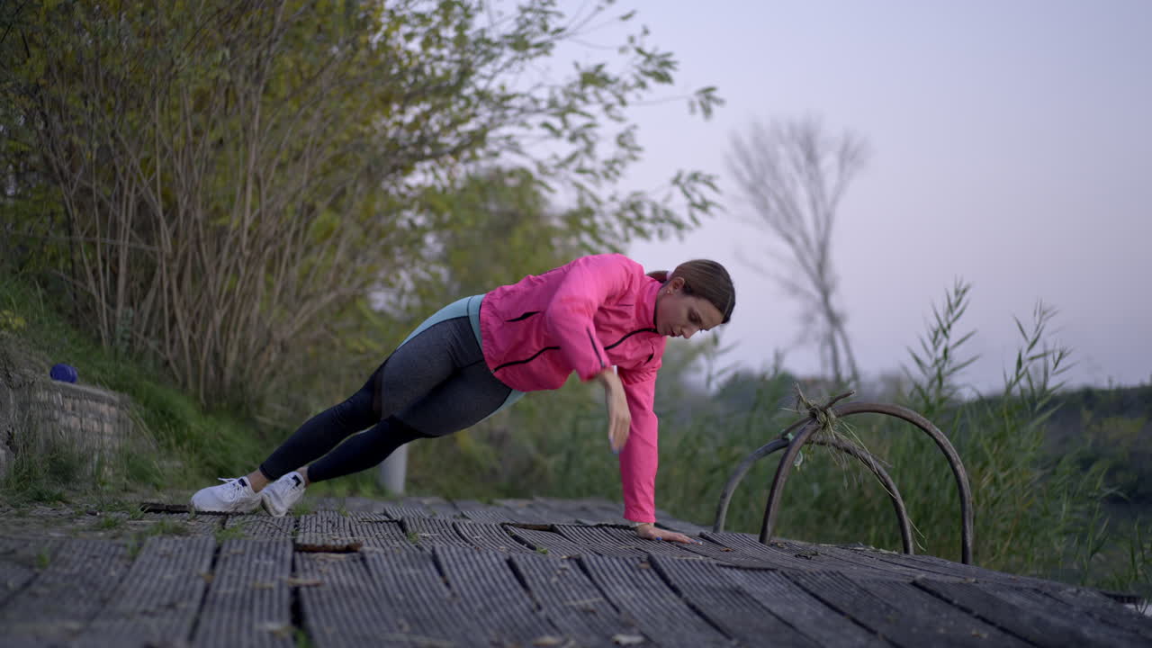 Woman working out outdoors, performing planks and push-ups on a pier