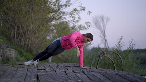 woman working out outdoors, performing planks and push-ups on a pier