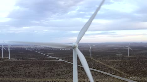 Aerial-closeup,-wind-turbine-turning,-landscape-of-a-field-of-turbines,-clean-renewable-energy,-blue-cloudy-sky