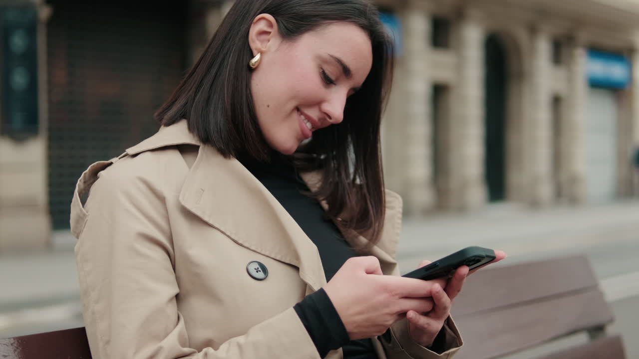 Giovane donna sorridente che usa lo smartphone su una panchina cittadina