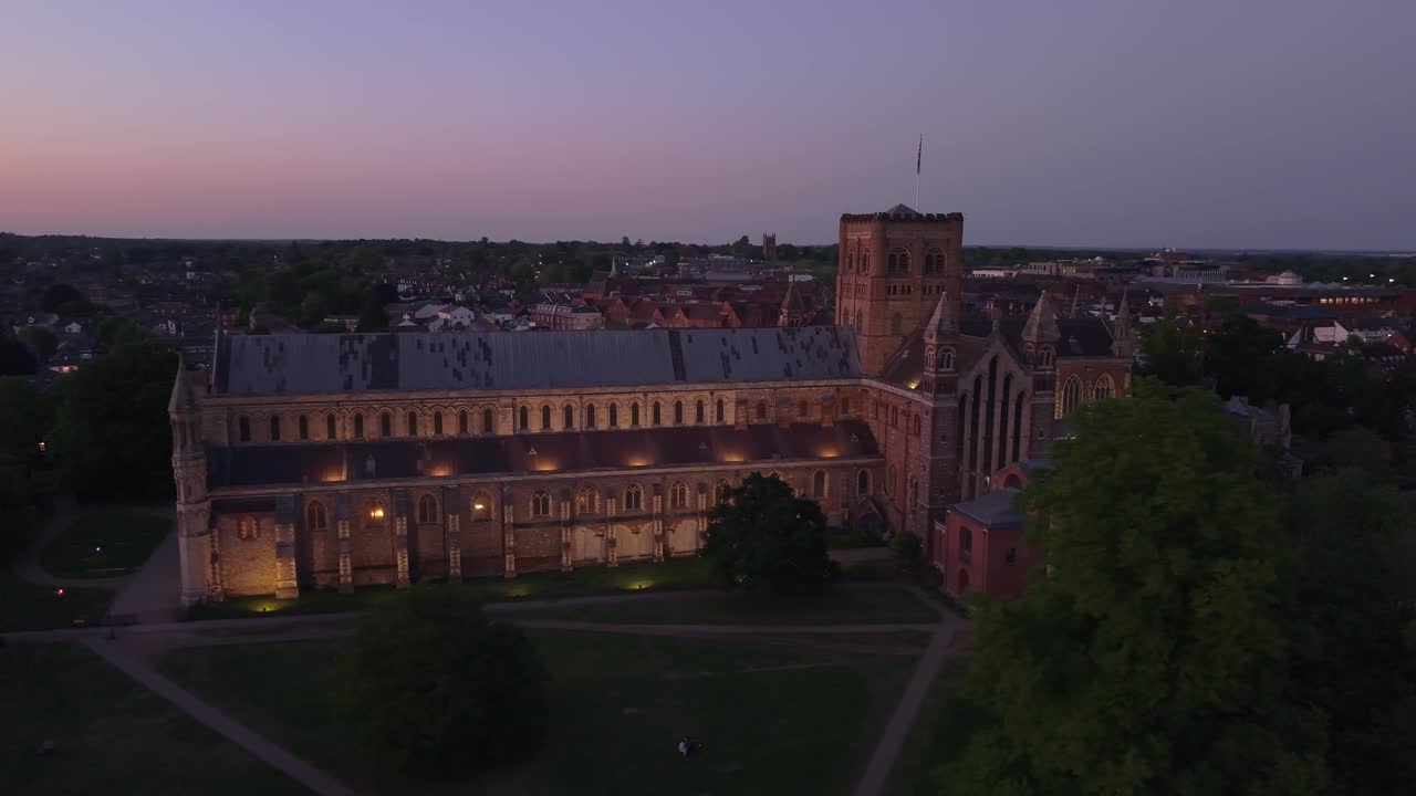 Dramatic close-up orbit drone footage of St Albans Cathedral glowing at twilight against a vivid orange evening sky