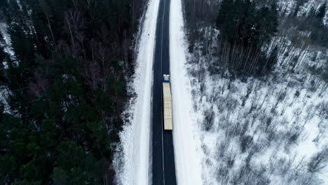 aerial view of loaded truck driving on the road through snowy pine forest in winter