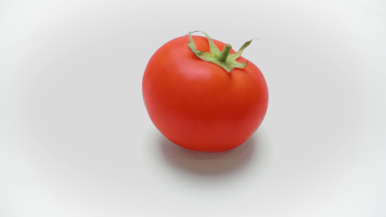 Small red tomato rotating on white background