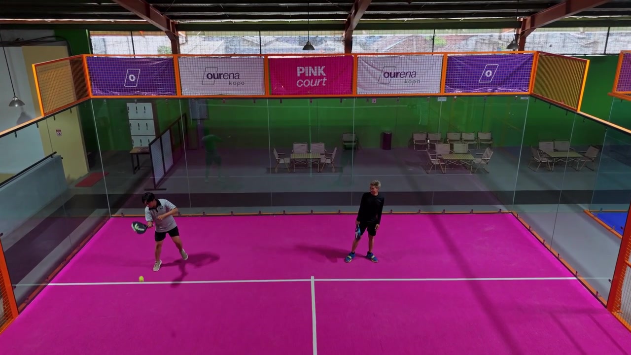 Drone view of padel tennis players moving on bright pink indoor court.