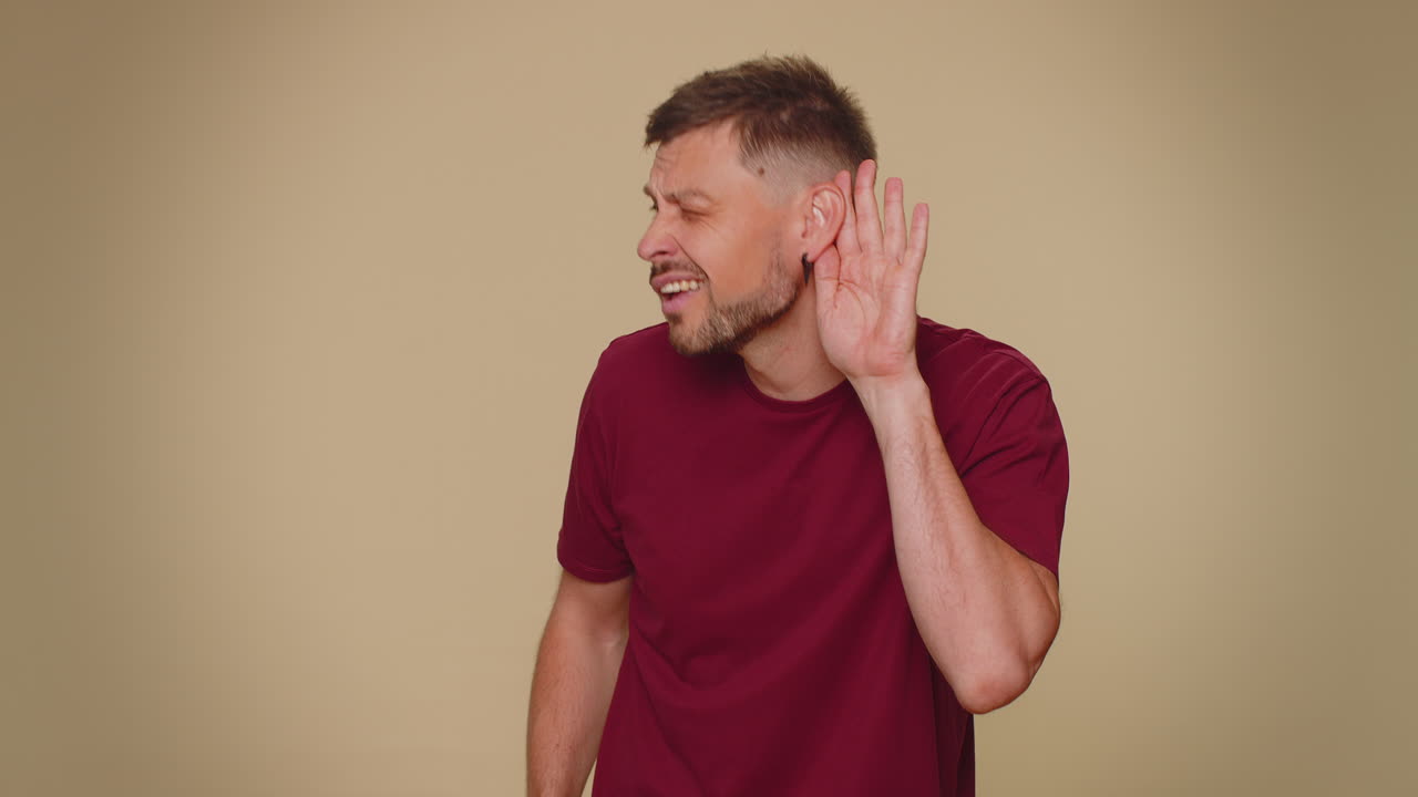 joven tratando de oírte, mirando confundido y fruncido el ceño, manteniendo el brazo cerca de la oreja para una voz más alta