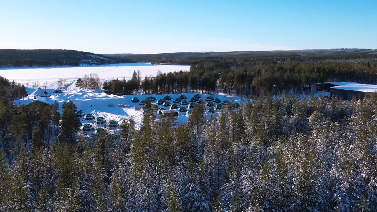 Aldea de iglús nevada capturada por dron, situada en medio de un tranquilo bosque finlandés.