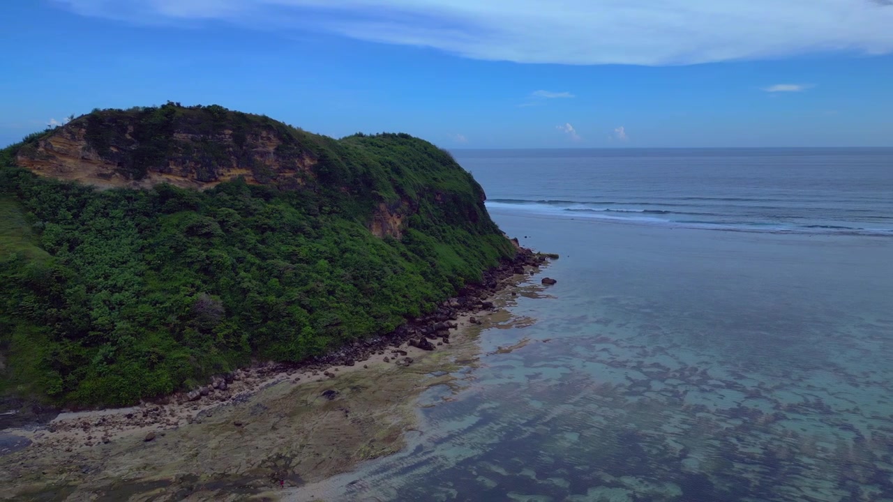 Scogliera verde lussureggiante che si affaccia sull'oceano blu limpido con piccole onde che si infrangono, suggerendo una destinazione tropicale. Fantastica vista aerea con rotazione panoramica a sinistra da drone