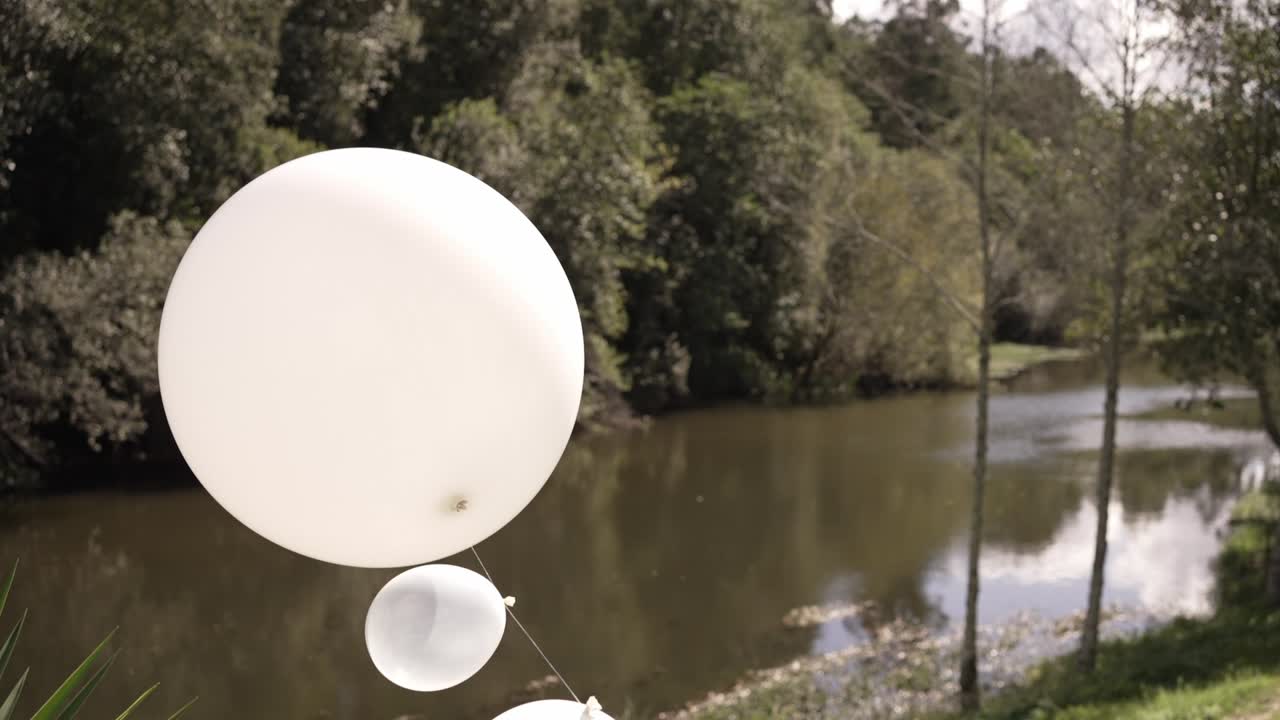 White balloons floating near a peaceful river with a wooded backdrop