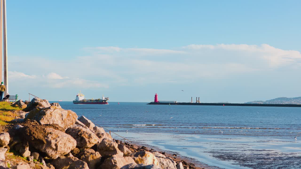 Farol de Poolbeg junto ao mar em dia claro com ondulações suaves e navio passando