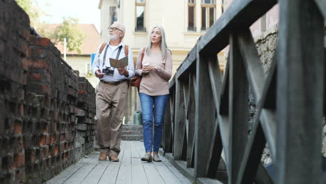 view from below of senior couple with a map and coffee walking a narrow bridge